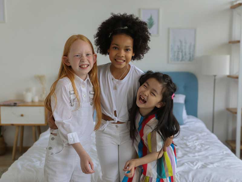 three children of differing ethnicities on a bed