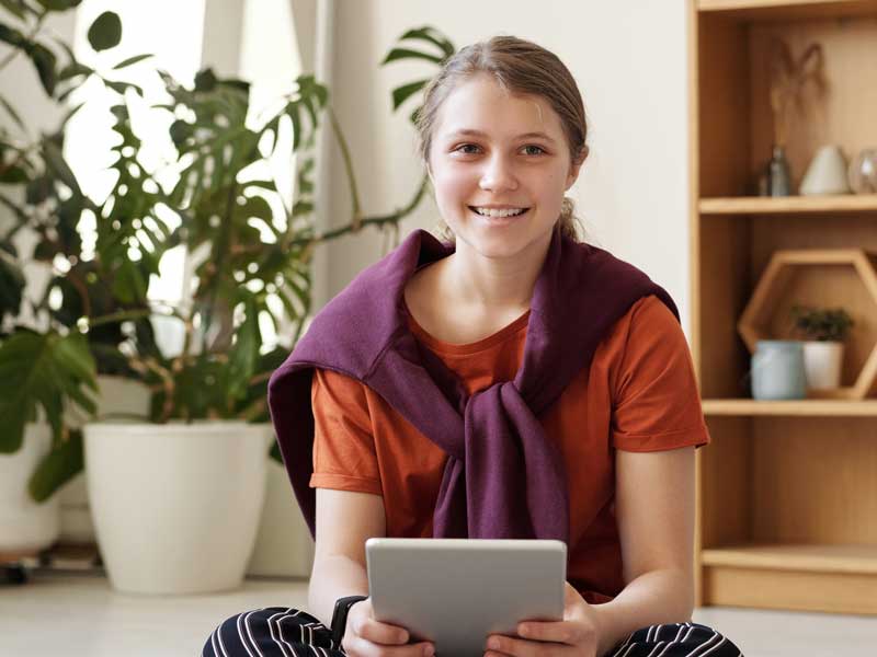 a smiling teenager sitting on the floor with a tablet computer