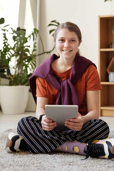 a smiling teenager sitting on the floor with a tablet computer